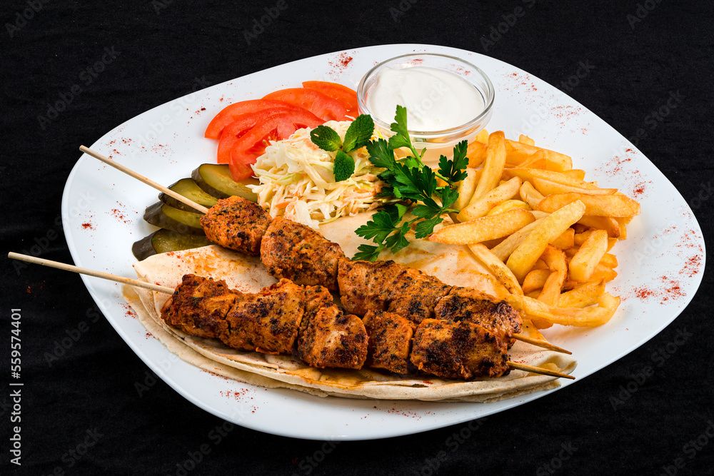 Kebab, barbecued chicken on a stick with tomatoes, french fries, potatoes, coleslaw, pickles, tortilla and sauce in a plate. Kebab, barbecued chicken on a stick with tomatoes, french fries, potatoes, coleslaw, pickles, tortilla and sauce in a plate.