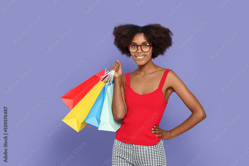 Happy African American woman in glasses with shopping bags on purple background Happy African American woman in glasses with shopping bags on purple background