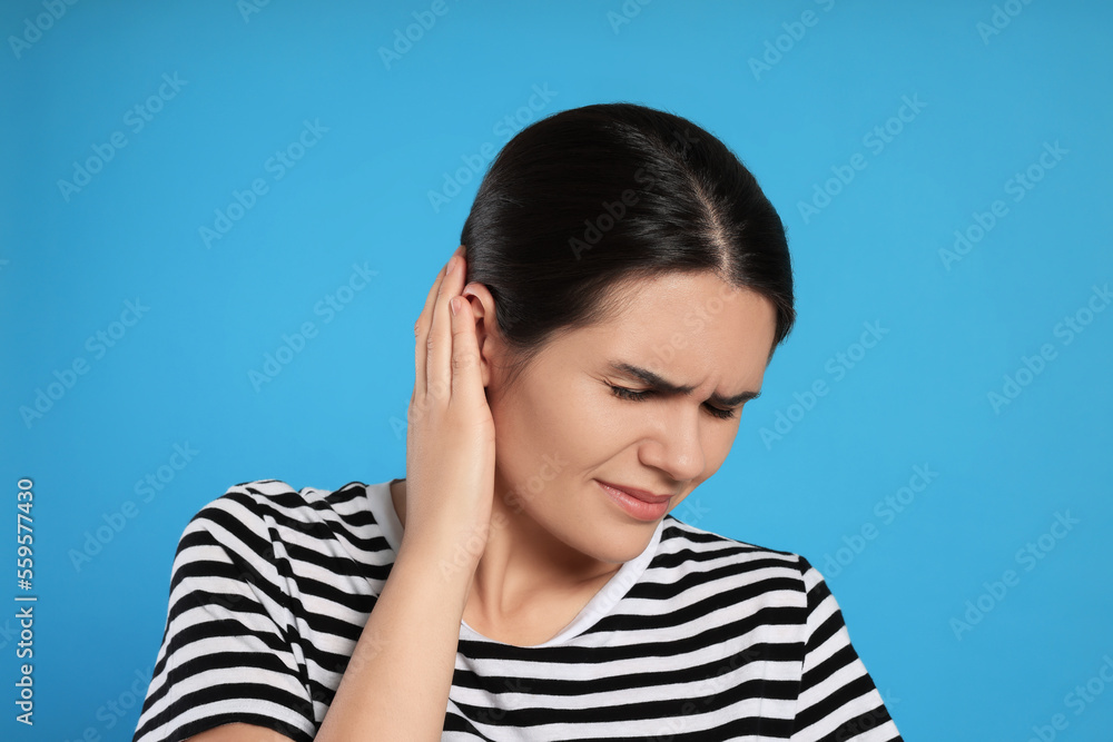 Young woman suffering from ear pain on light blue background Young woman suffering from ear pain on light blue background