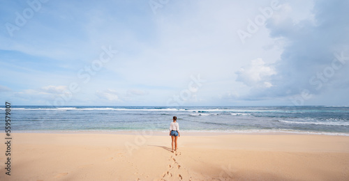 Vacation on the shore. Young woman standing on tropical beach enjoying beautiful view.