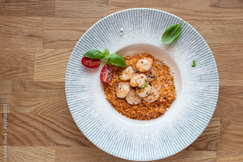 Tomato risotto with shrimps and basil on a wooden table. Top view, selective focus. Tomato risotto with shrimps and basil on a wooden table. Top view, selective focus.