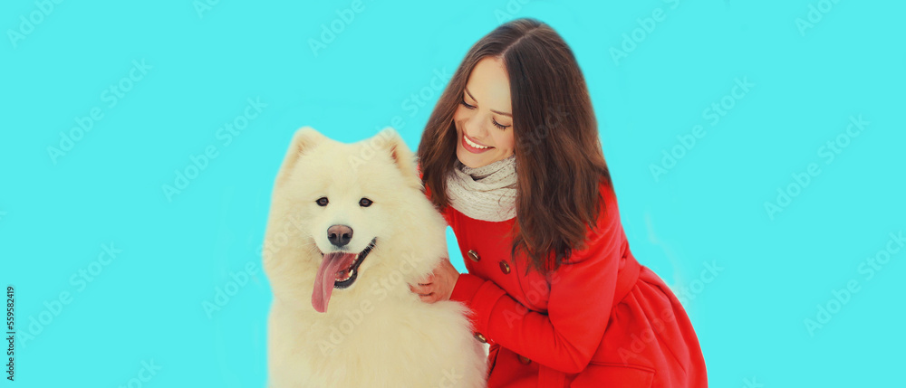 Portrait of happy smiling young woman owner with white Samoyed dog on blue background