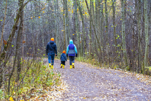 Father, mother and son walk away along the autumn road.