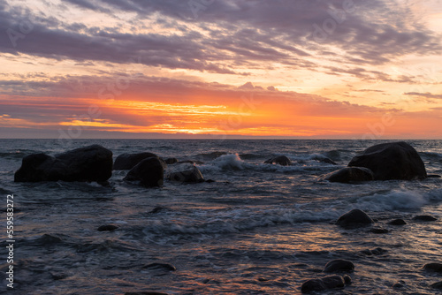 Rocks by the ocean with waves and dramatic sky at sunrise. 