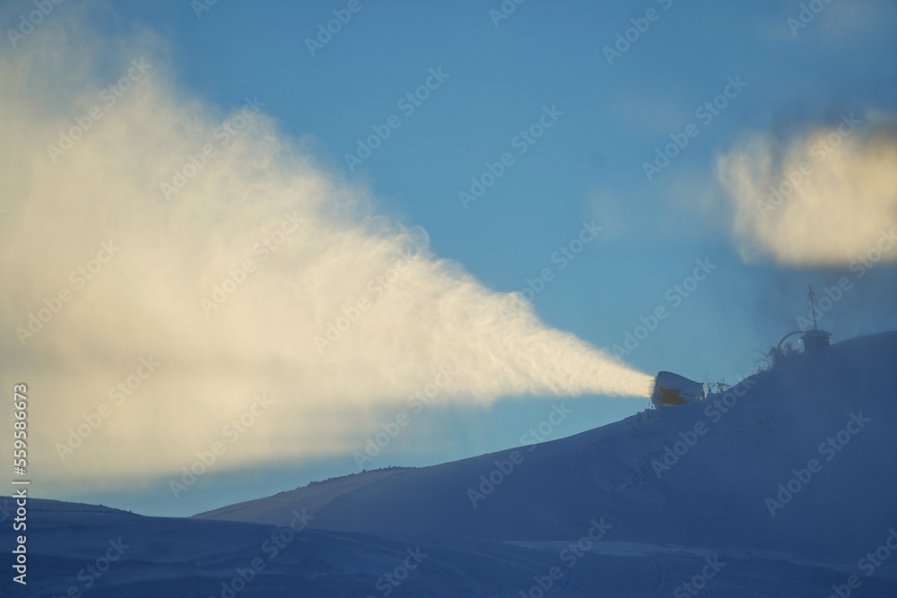Fototapeta premium Snow cannon in winter mountains. Snow-gun spraying artificial ice crystals. Machine making snow