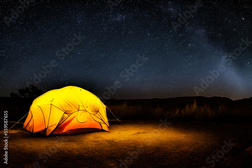 Night camping underneath the stars. Tent illuminated by light. High contrast with starry night sky. Hiking