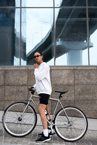 Fit and stylish african american woman standing near bike on street 