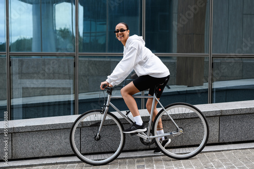 Positive african american woman in sunglasses cycling outdoors 