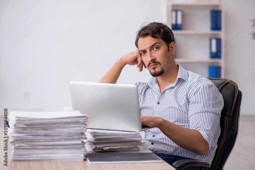 Young male employee unhappy with excessive work in the office Young male employee unhappy with excessive work in the office