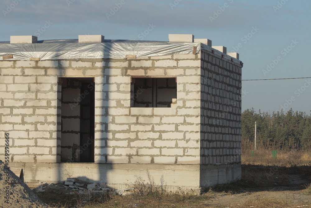 part of one white brick unfinished house on the street in the grass against the blue sky part of one white brick unfinished house on the street in the grass against the blue sky