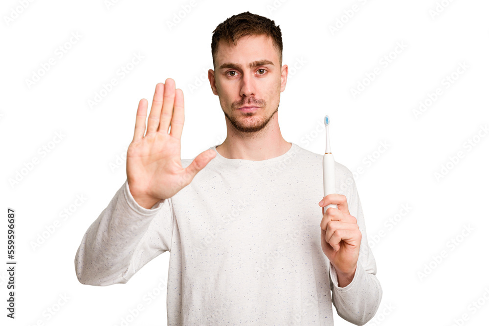 Young caucasian man holding an electric toothbrush isolated cut out standing with outstretched hand showing stop sign, preventing you. Young caucasian man holding an electric toothbrush isolated cut out standing with outstretched hand showing stop sign, preventing you.