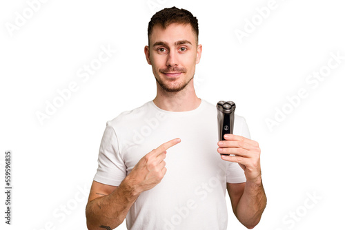 Young man holding a shaving machine cut out isolated smiling and pointing aside, showing something at blank space.