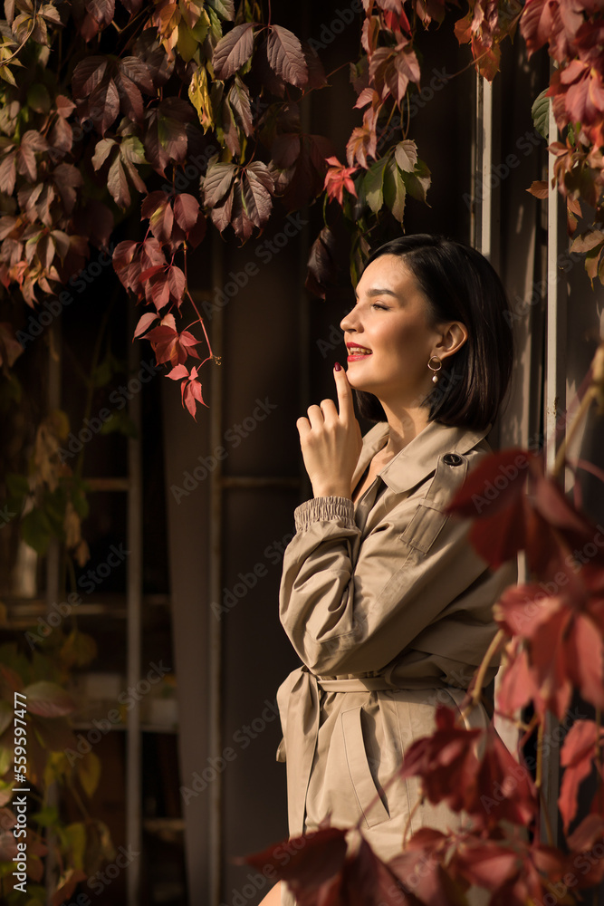 a beautiful brunette woman in a coat by the hedge braided with autumn vines.