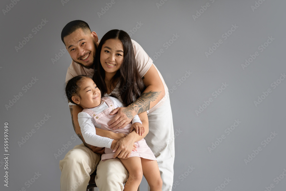 Cheerful asian family with toddler daughter looking at camera isolated on grey background 