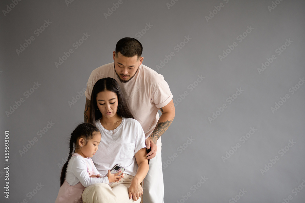 Young asian parents looking at toddler daughter with smartphone isolated on grey background Young asian parents looking at toddler daughter with smartphone isolated on grey background