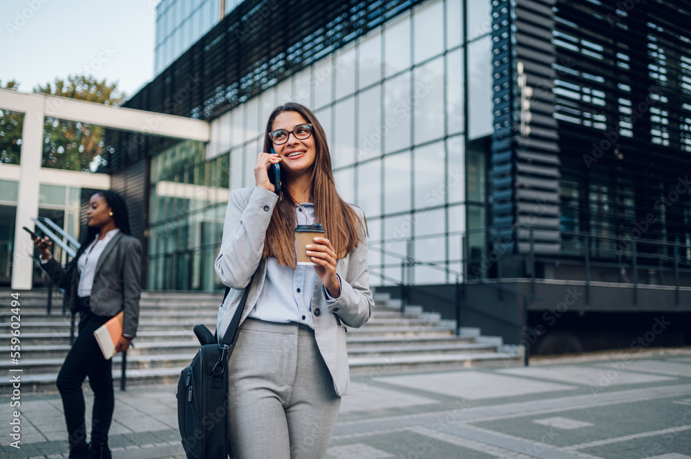 Business woman standing outside while using a smartphone and drinking coffee Business woman standing outside while using a smartphone and drinking coffee