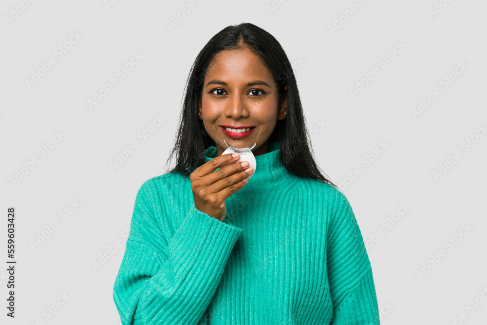 Young Indian woman holding a teeth whitener isolated on white background