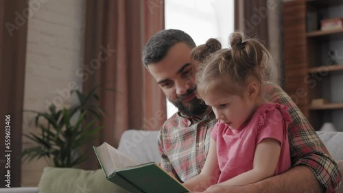 Young father and daughter read intersting book at home. Loving parent bearded man teaches his preschool child to read. Daddy reading fairy tale story. Parenthood, love and happy family concept. photo