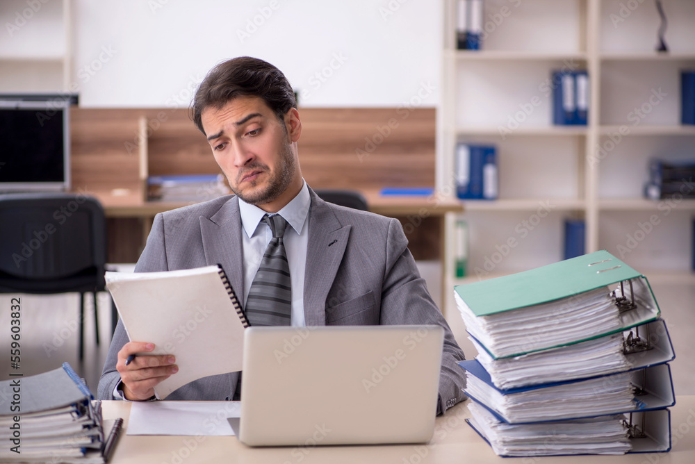 Young male employee unhappy with excessive work in the office Young male employee unhappy with excessive work in the office