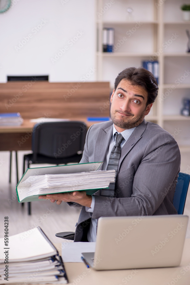 Young male employee unhappy with excessive work in the office Young male employee unhappy with excessive work in the office