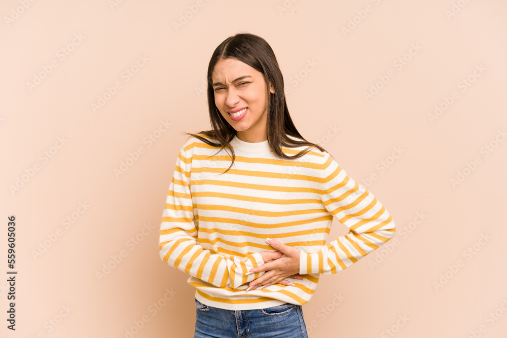 Young colombian woman isolated on beige background having a liver pain, stomach ache. Young colombian woman isolated on beige background having a liver pain, stomach ache.