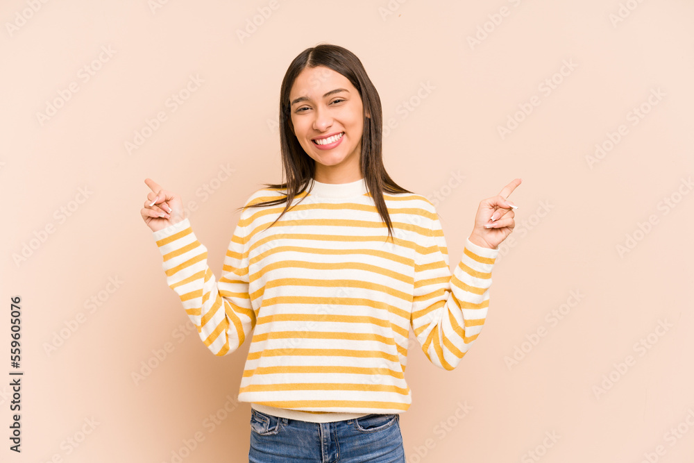 Young colombian woman isolated on beige background pointing to different copy spaces, choosing one of them, showing with finger. Young colombian woman isolated on beige background pointing to different copy spaces, choosing one of them, showing with finger.
