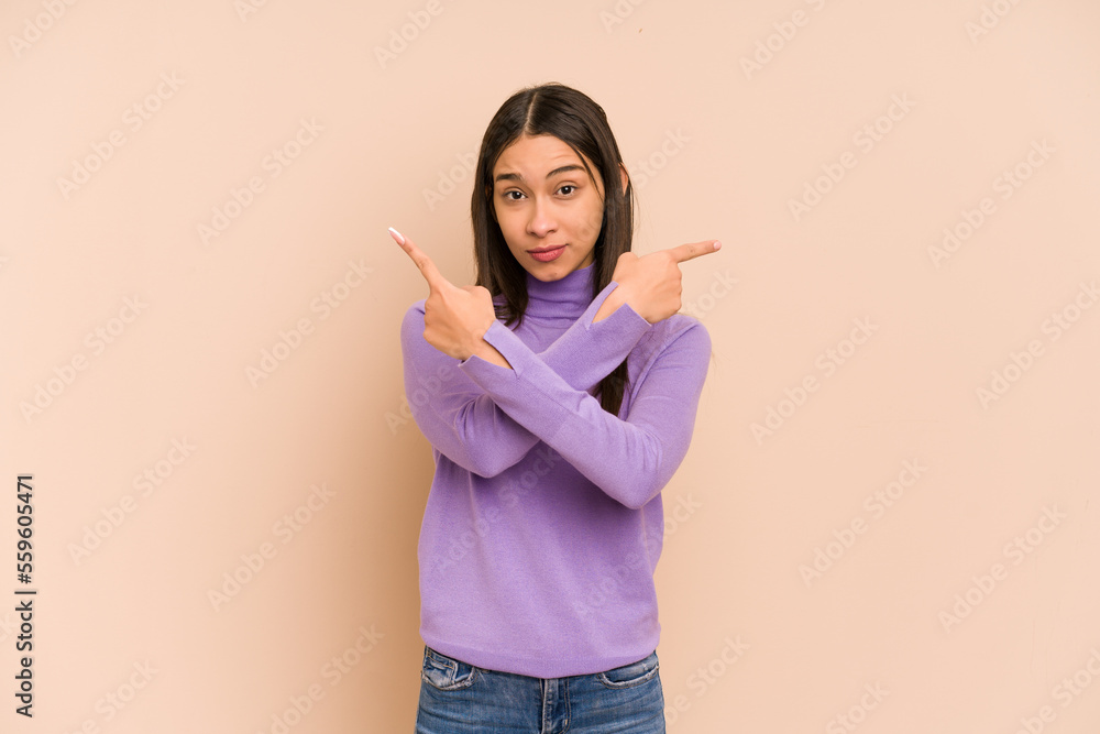 Young colombian woman isolated on beige background points sideways, is trying to choose between two options. Young colombian woman isolated on beige background points sideways, is trying to choose between two options.