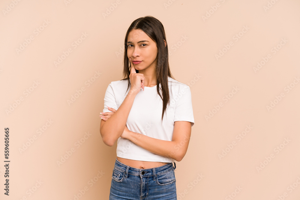 Young colombian woman isolated on beige background looking sideways with doubtful and skeptical expression. Young colombian woman isolated on beige background looking sideways with doubtful and skeptical expression.
