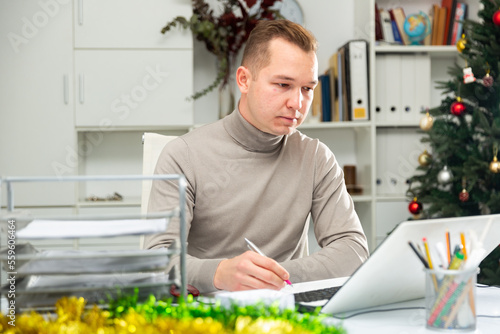 Male office worker sitting at desk and doing paperwork during Christmastime. © JackF