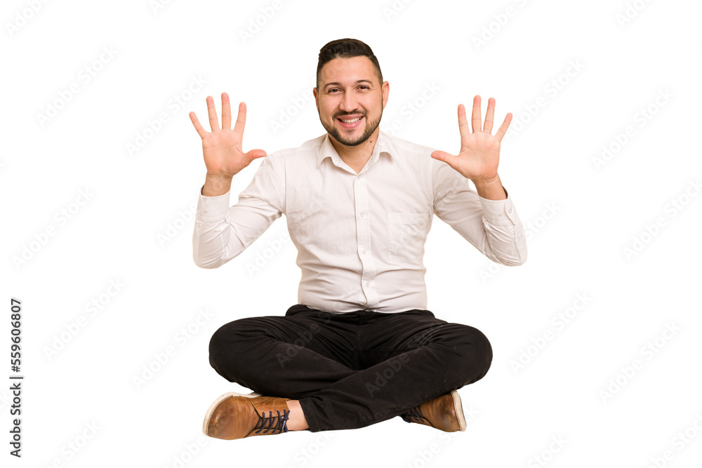Adult latin man sitting on the floor cut out isolated showing number ten with hands. Adult latin man sitting on the floor cut out isolated showing number ten with hands.