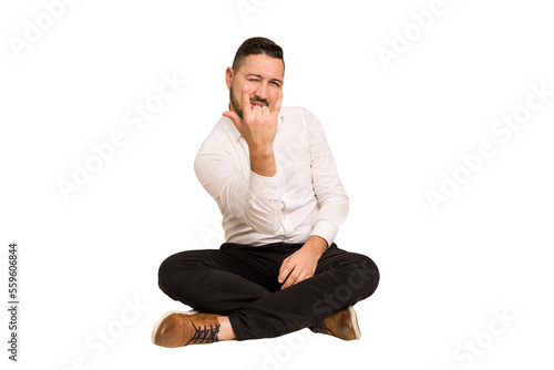 Adult latin man sitting on the floor cut out isolated showing rock gesture with fingers © Asier