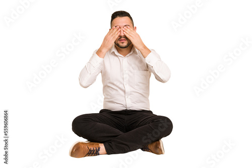 Adult latin man sitting on the floor cut out isolated afraid covering eyes with hands.