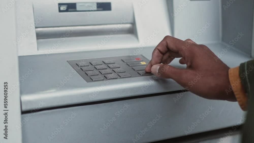 Close-up view of young African-American man's hands entering pincode of bank card using ATM terminal to make financial operations. Adult African male making transactions outdoors. Close-up view of young African-American man's hands entering pincode of bank card using ATM terminal to make financial operations. Adult African male making transactions outdoors.