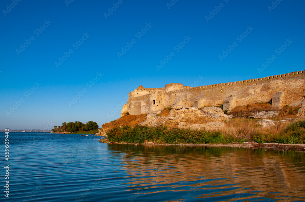 Old stone fortress on the shore of the lake. Beautiful sunny landscape with fortress and blue sky
