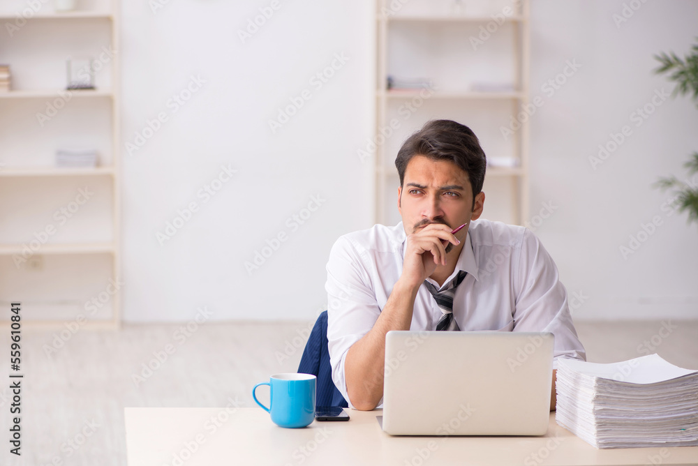 Young male employee unhappy with excessive work in the office Young male employee unhappy with excessive work in the office