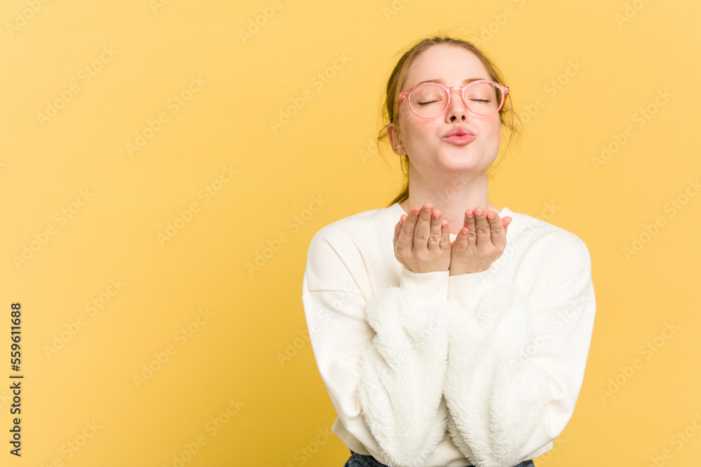Young caucasian redhead woman isolated on yellow background folding lips and holding palms to send air kiss. Young caucasian redhead woman isolated on yellow background folding lips and holding palms to send air kiss.