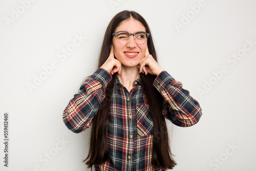 Young caucasian woman isolated on white background covering ears with fingers, stressed and desperate by a loudly ambient. © Asier