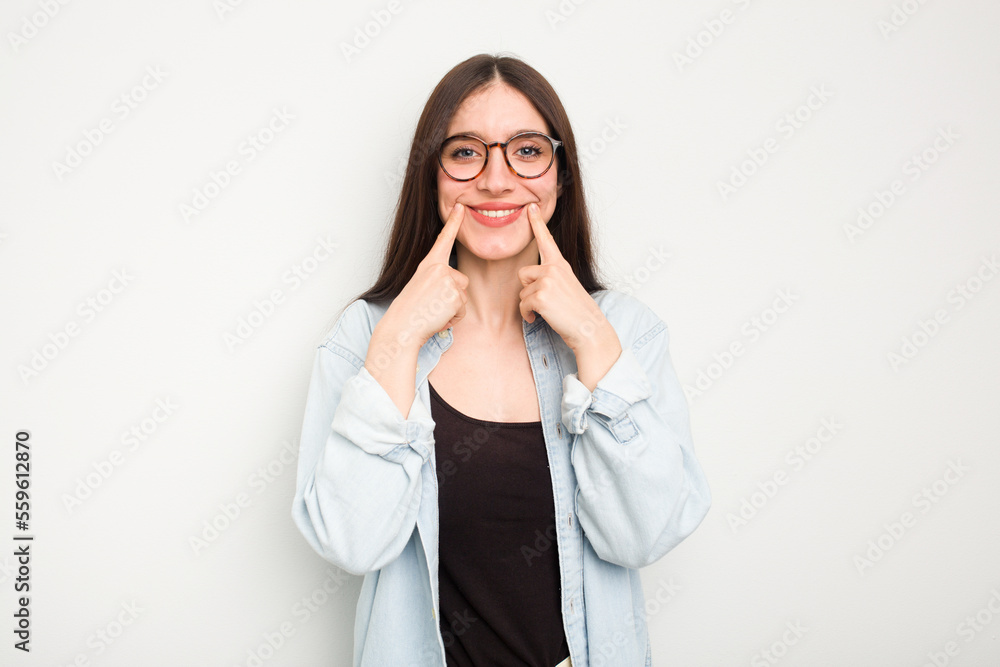 Young caucasian woman isolated on white background smiles, pointing fingers at mouth. Young caucasian woman isolated on white background smiles, pointing fingers at mouth.