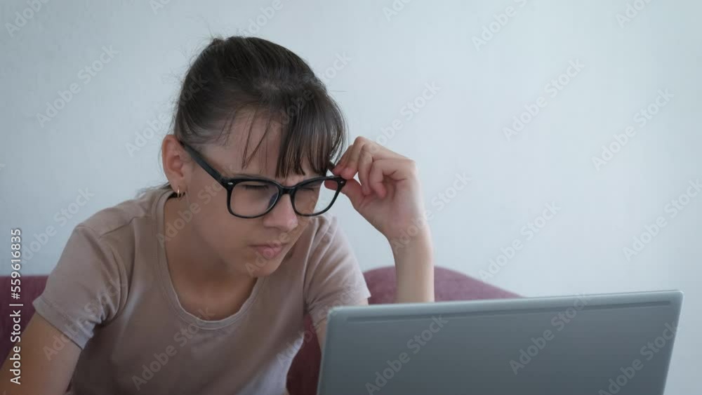 Squinting eyes and looking to laptop. A view of teen in glasses try to work online and have tired eyes because of health problems. Squinting eyes and looking to laptop. A view of teen in glasses try to work online and have tired eyes because of health problems.
