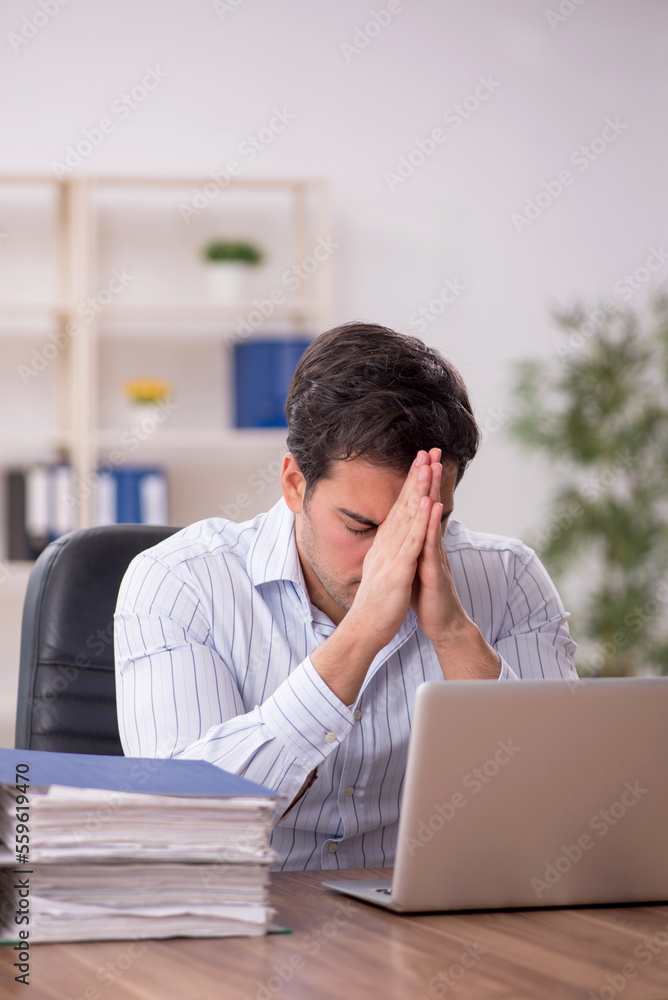 Young male employee and too much work in the office Young male employee and too much work in the office