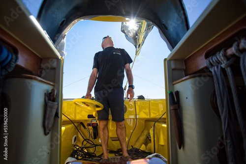 Man looking up while standing on sailboat during preparation for race, La Trinite-sur-Mer, Morbihan, France photo