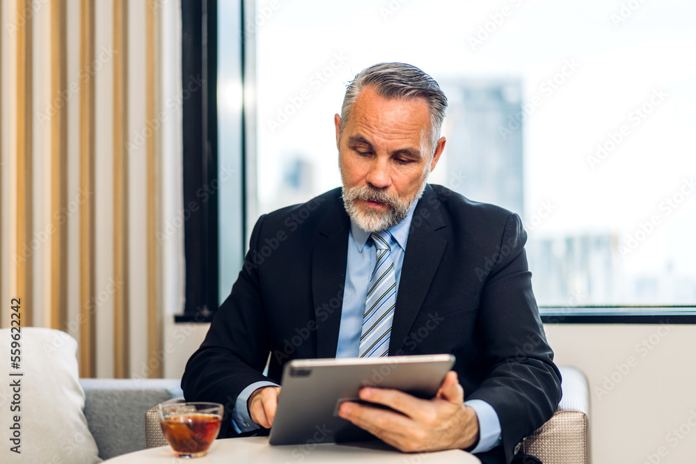 Handsome confident senior businessman relaxing use technology of tablet computer while sitting on chair.elderly creative coworkers business people working and use tablet at office Handsome confident senior businessman relaxing use technology of tablet computer while sitting on chair.elderly creative coworkers business people working and use tablet at office