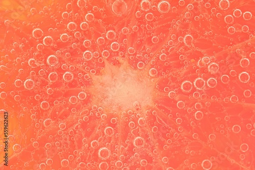 Close-up of a grapefruit slice in liquid with bubbles. Slice of red ripe grapefruit in water. Close-up of fresh grapefruit slice covered by bubbles