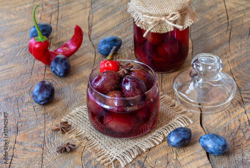Homemade Sweet and Sour Spiced pickled plums in marinade with star anise, bay leaf and chilli pepper in a glass jar. Wooden table, selective focus, horizontal. photo