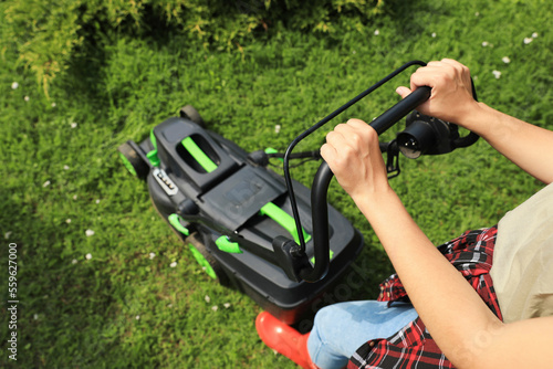 Woman cutting grass with lawn mower in garden, above view