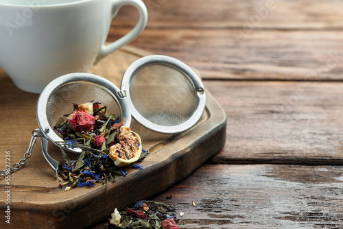 Snap infuser with dried herbal tea leaves and fruits on wooden table, closeup. Space for text
