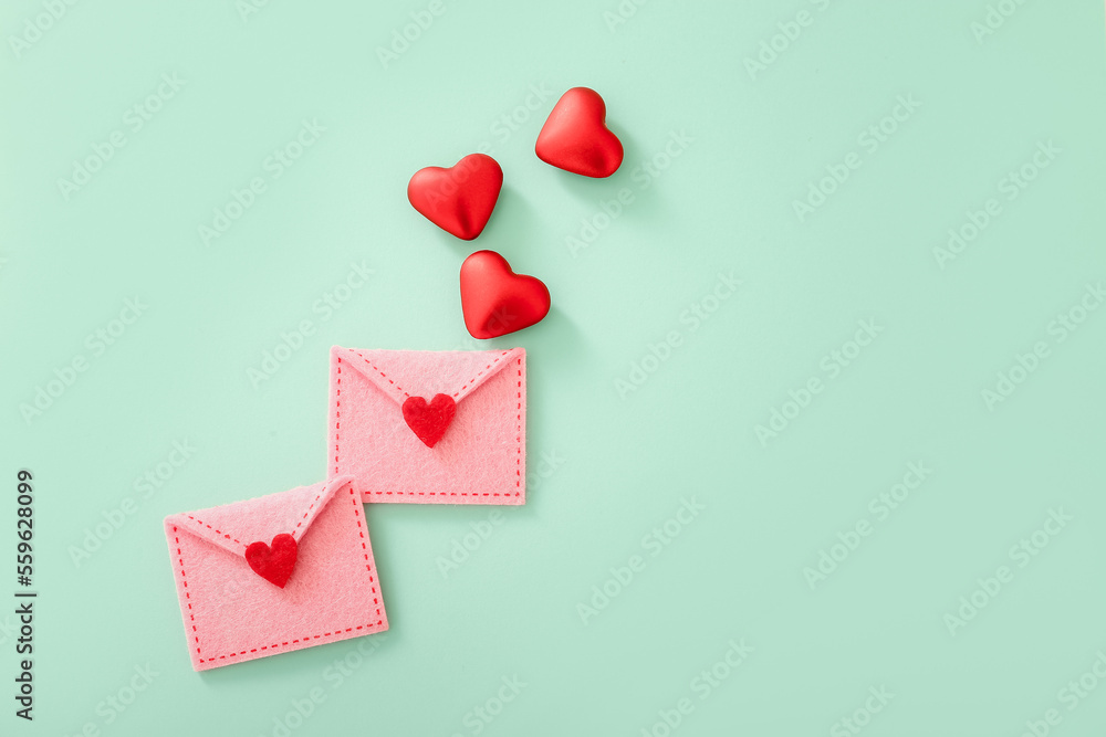 Felt envelopes with red hearts for Valentine day on color background, top view