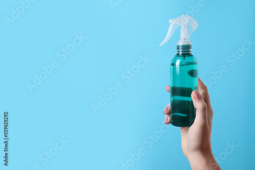 Woman holding spray bottle with thermal protection on light blue background, closeup. Space for text