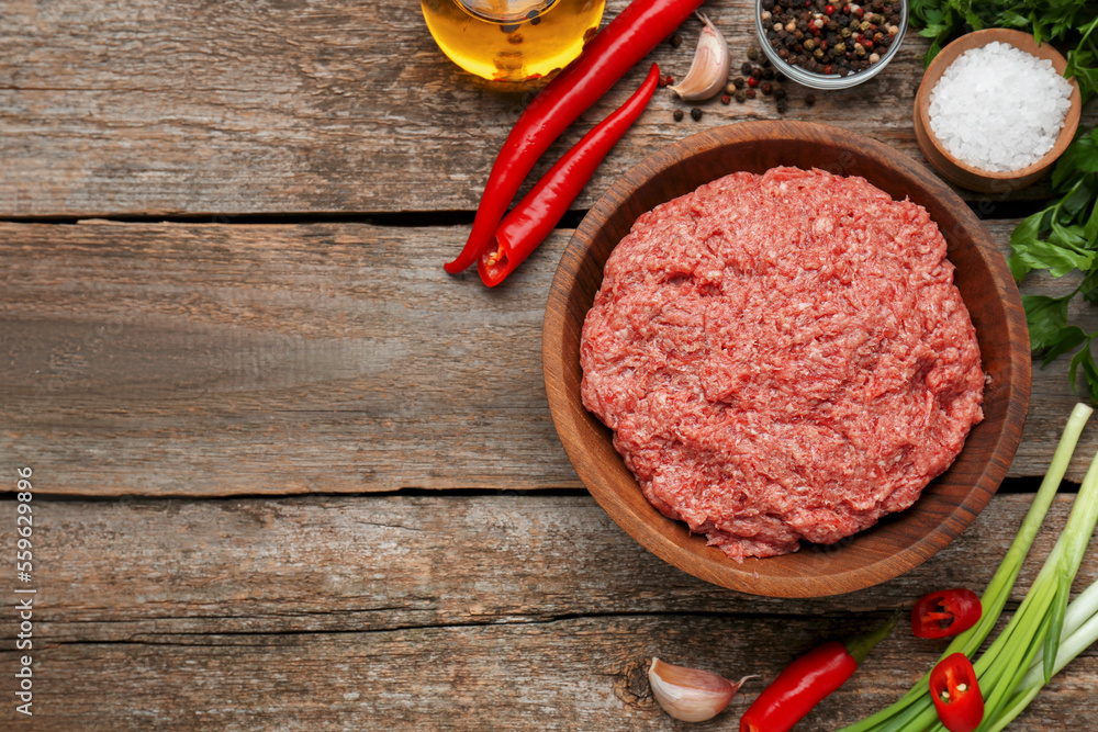 Bowl with raw fresh minced meat and ingredients on wooden table, flat lay. Space for text Bowl with raw fresh minced meat and ingredients on wooden table, flat lay. Space for text