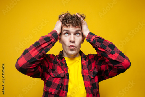 surprised guy with curly hair holds his hair with his hands and looks up, the guy is doing the styling